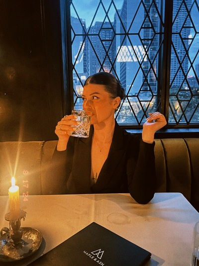 woman at a low lit bar sipping on cocktail with her hair slicked backed into a low bun hairstyle