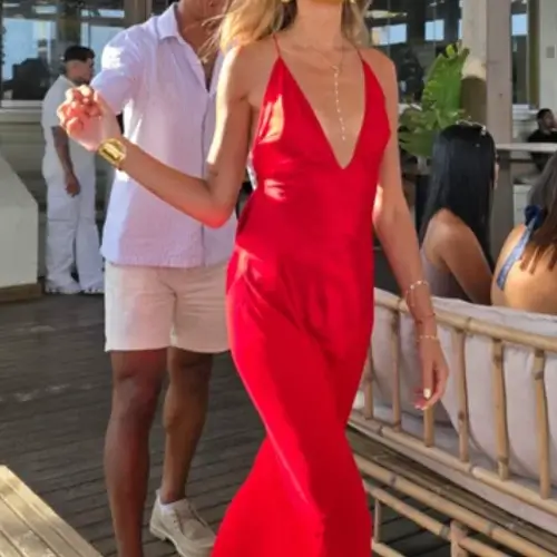 Young blonde woman wearing vibrant red stain maxi dress with plunging neckline walking hand in hand with date
