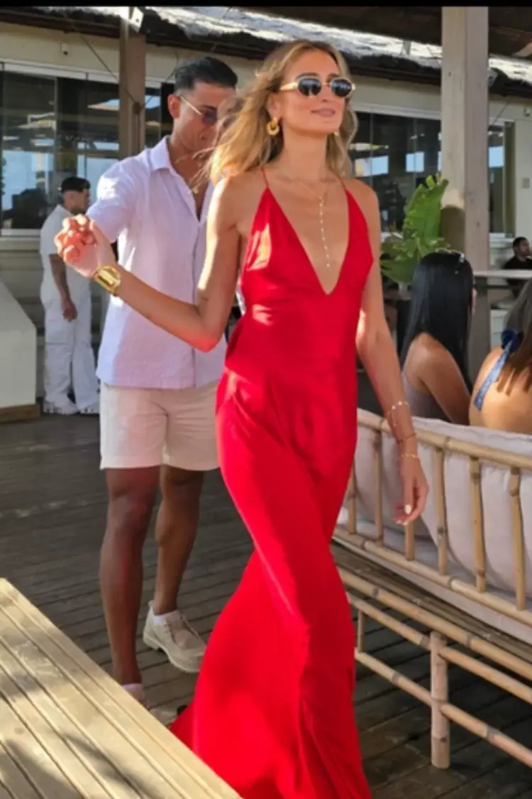 Young blonde woman wearing vibrant red stain maxi dress with plunging neckline walking hand in hand with date