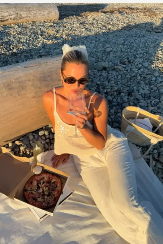 young woman attending a beach date laying on blanket wearing all white ensemble with a sequin top and linen pants