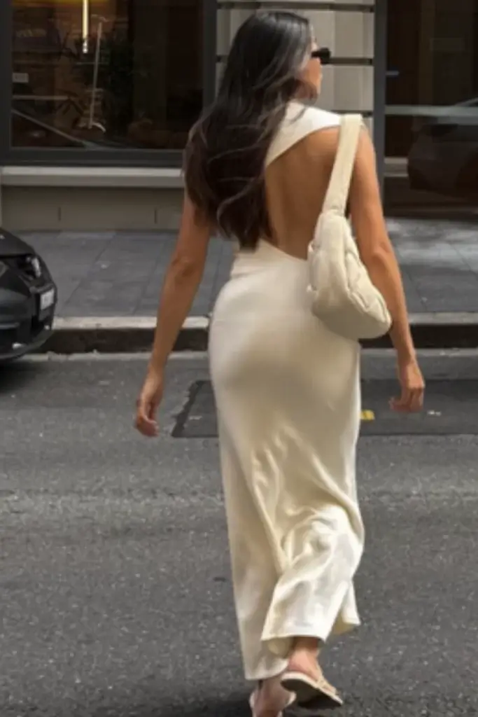 woman walking across city street wearing asymmetrical open back white maxi dress and kitten heels