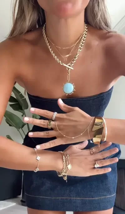 young woman showing off full hand and neck of gold accessories and jewelry