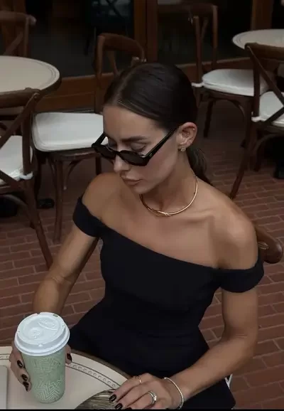chic dressed woman sitting at cafe table drinking coffee drink