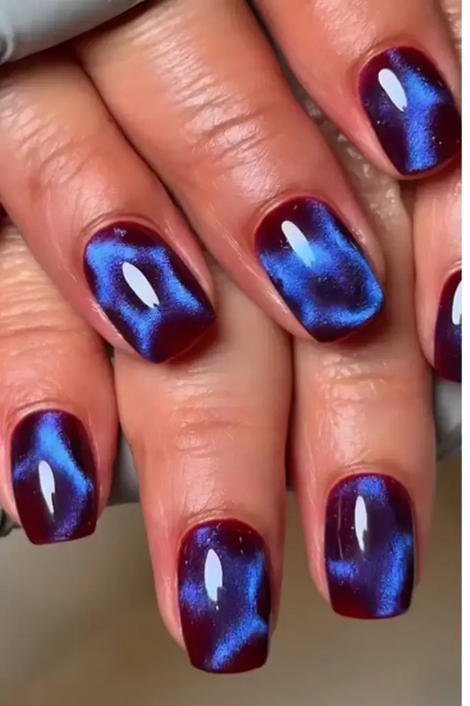 short nails with a dark burgundy based and metallic blue cat eye gel effect on top