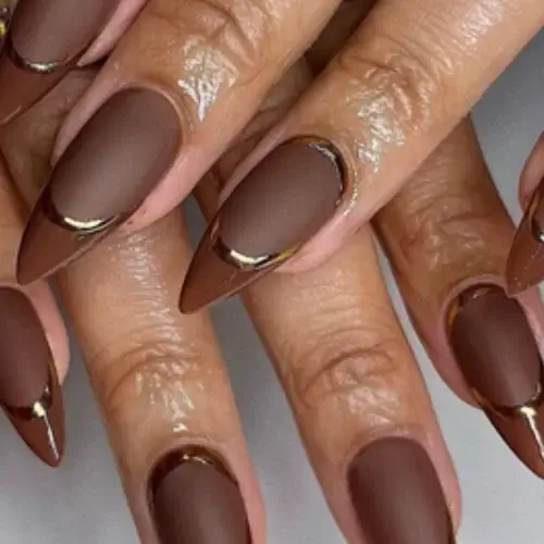classy dark fall nail designs on woman's hand featuring different shades of brown french manicure with gold accents