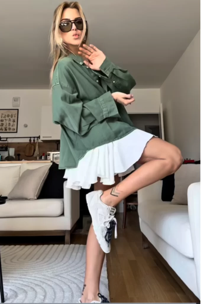 Warm Weather Fall outfit idea with oversized button down in olive green paired with a ruffle white mini skirt worn on a blonde woman casually with sneakers