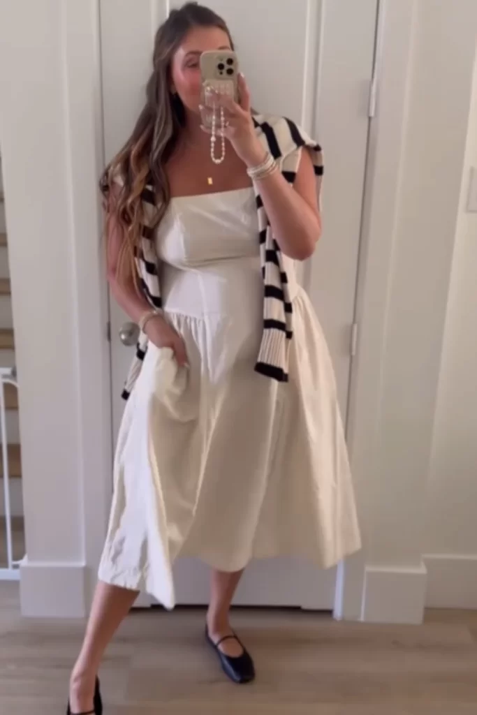woman wearing white maxi cotton dress with a striped sweater draped over shoulders and leather ballet flats