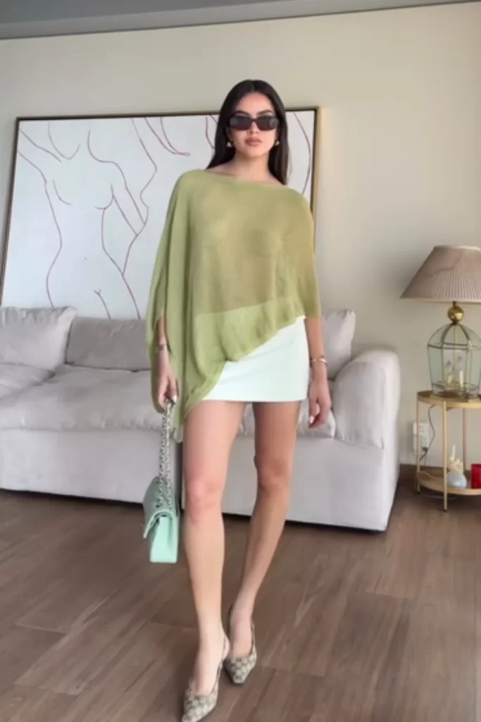 woman wearing ligthweight olive green asymmetrical poncho over a white mini skirt