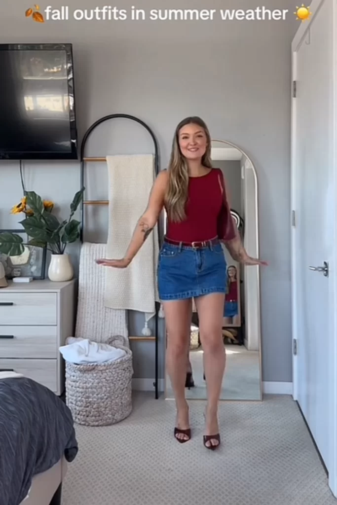 young blonde woman in room wearing burgundy color tank, and denim mini skirt as a warm weather autumn outfit