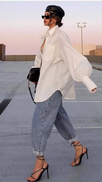 woman wearing dramatic oversized white button down paired with baggy jeans that are cuffed at the hem and showing sleek strappy black heels