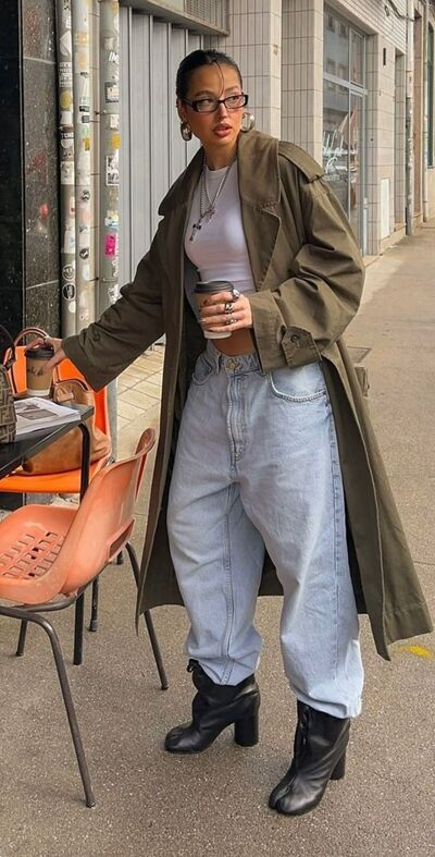 woman wearing baggy jeans tucked into leather ankle boots paired with white crop top and olive green trench coat to balance proportions 