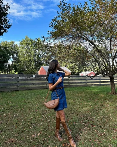 Woman wine tasting at vineyard in Fall season wearing dark denim mini dress and brown boots