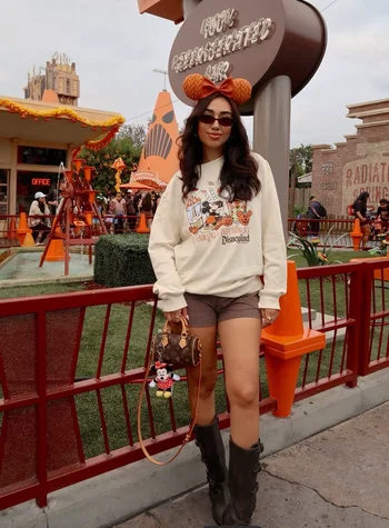 Young woman at disneyland during Fall wearing Disney pull over and plaid shorts with boots